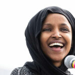 Smiling woman in hijab speaking into a microphone.