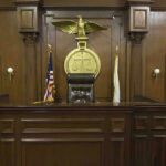 Billionaire’s ALLEGED Court Meddling: Truth OR Tactic? Judges bench in an empty courtroom, scales emblem above.