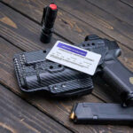 Pistol, holster, permit, flashlight, and magazine on wooden background.