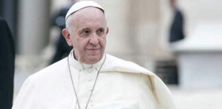 Man in white religious robe and cap outdoors.