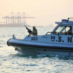 U.S. Navy patrol boat on water near industrial port.