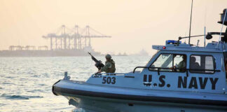 U.S. Navy patrol boat on water near industrial port.