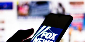 Silhouette hand holding phone displaying Fox News logo.