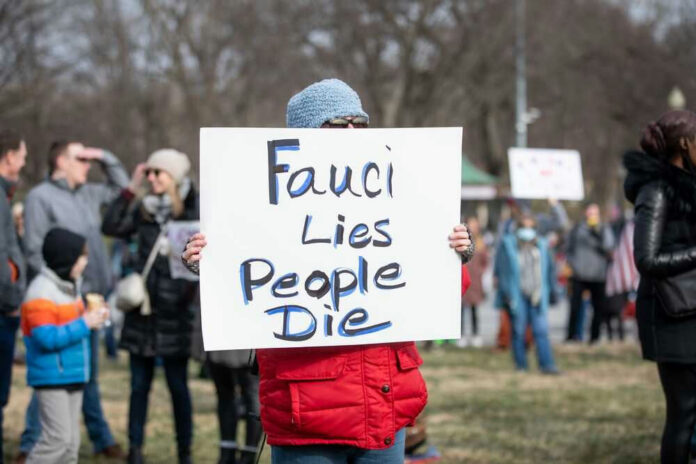 Person holding sign that reads Fauci Lies People Die