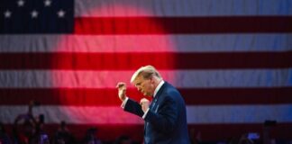A speaker gesturing passionately in front of an American flag at a rally