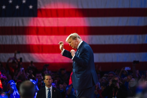 A speaker gesturing passionately in front of an American flag at a rally