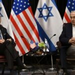Two political leaders seated with flags in the background