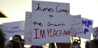 Protestors with signs, central sign references James Comey.