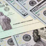 Economic Impact Payment check surrounded by hundred-dollar bills.