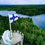 Nuclear Weapons Now Legal In Finland? Finnish flag flying on a stone tower above a forest and lake