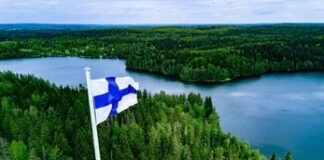 Finnish flag flying on a stone tower above a forest and lake