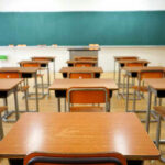 Empty classroom with wooden desks and chalkboard.