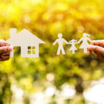Hands holding paper cutouts of house and family.