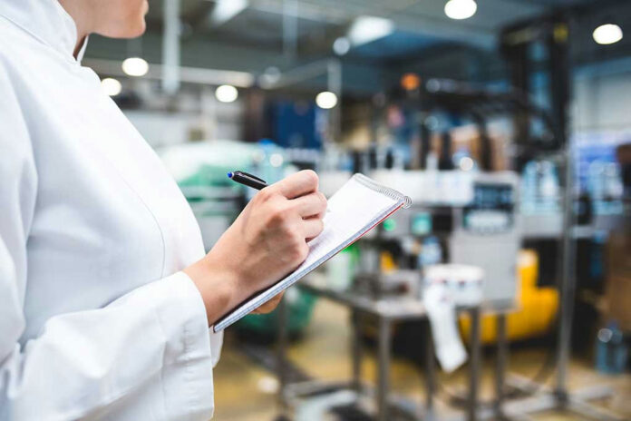 566863540 Person in lab coat writing on clipboard in factory.