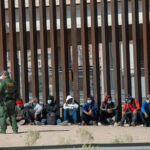 New Wall, SAME Old Tricks? Border patrol agent with group of seated immigrants.