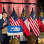 DeSantis Sidelined—Who’s Really Picking Florida’s Next Governor? Man speaking at Florida Blueprint event with American flags.