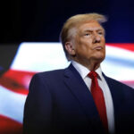 Trump BYPASSES Tehran — Stakes EXPLODE donald trump in suit with red tie American flag backdrop