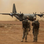 US Boots INSIDE Iran? Two soldiers watch a military transport plane on a dusty airstrip
