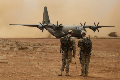 shutterstock350545301jpg Two soldiers watch a military transport plane on a dusty airstrip