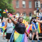 People celebrating at a pride parade, waving rainbow flags.