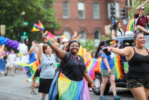 People celebrating at a pride parade, waving rainbow flags.