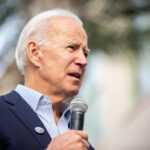 A man in a suit speaking into a microphone at an outdoor event