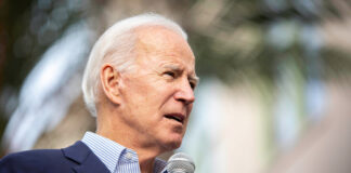 A man in a suit speaking into a microphone at an outdoor event