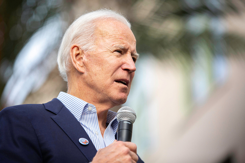 A man in a suit speaking into a microphone at an outdoor event