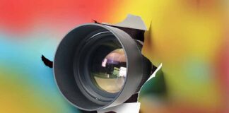 Camera lens emerging through torn paper