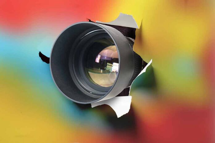 Camera lens emerging through torn paper