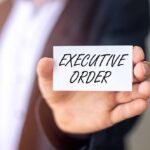 DEEP STATE Purge Begins Hand holding a small card with bold text in front of a blurred suit jacket