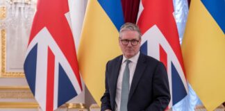 Man in suit stands before UK and Ukraine flags at a signing table