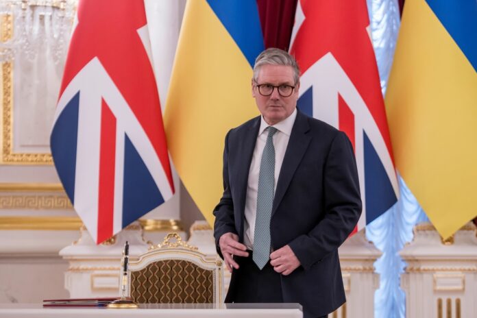 Man in suit stands before UK and Ukraine flags at a signing table