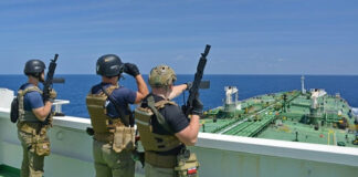 Armed security team on a ship deck overlooking a large tanker at sea