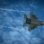 Jet fighter flying through a cloudy blue sky leaving vapor trails
