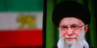 Person wearing glasses and turban in front of flag