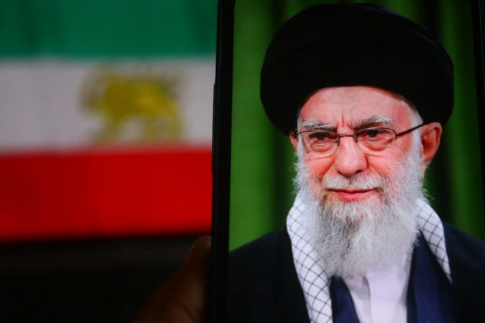 Person wearing glasses and turban in front of flag