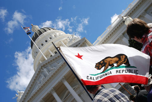 California state flag waving near a white domed capitol building