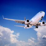 Commercial airplane flying with landing gear extended against a blue sky