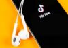 DOJ Greenlights TikTok — What Changed? Smartphone with TikTok app and white wired earbuds on yellow background