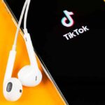 Smartphone with TikTok app and white wired earbuds on yellow background