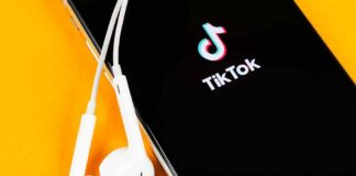 Smartphone with TikTok app and white wired earbuds on yellow background