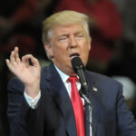 A man speaking into a microphone with a hand gesture during a speech