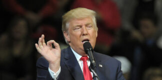 A man speaking into a microphone with a hand gesture during a speech