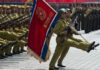 Soldiers march in formation carrying a red military flag