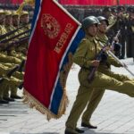 Putin Thanks North Korea For Troops Soldiers march in formation carrying a red military flag