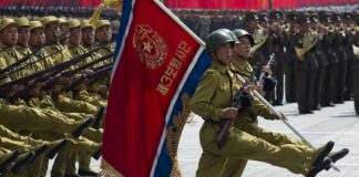 Soldiers march in formation carrying a red military flag