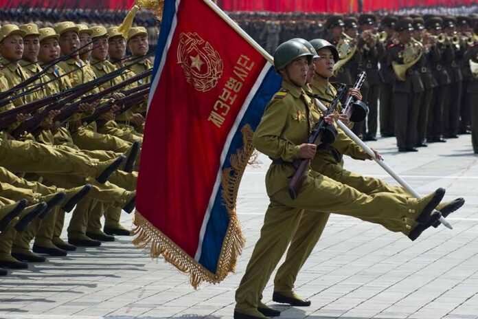 shutterstock_148621262 Soldiers march in formation carrying a red military flag