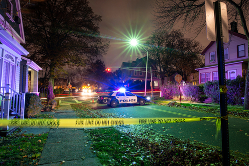Police car with flashing lights at a crime scene surrounded by caution tape