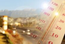 Close-up of a thermometer in hot sun over a blurred road and mountains